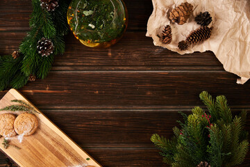 Wooden background, craft paper, cookies, herbal tea and spruce branches, holiday composition