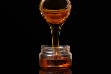Natural honey from the jar flows to the bottom on a black background.