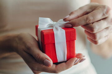 Close-up of female hands holding a small gift wrapped with a satin ribbon