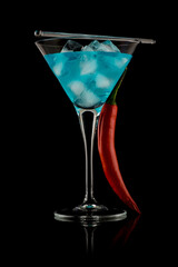 Martini glass filled with clear blue liquid. Cocktail. Red pepper leaning on the glass. Studio photo isolated on black background. Reflective surface.