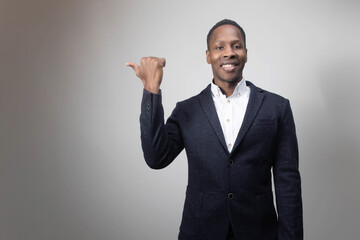 Look at this! Handsome young African man pointing up and smiling to you while standing against grey background