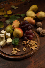 Wine snacks set: selection of cheese, grapes, pear and walnuts on a wooden board. Appetizer plate with fruits, grapes, nuts on a dark wooden plate and wooden table.