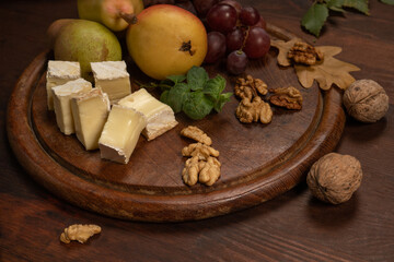 Cheese plate with fruits, grapes, nuts on a dark wooden plate and wooden table. Wine snacks set: selection of cheese, grapes, pear and walnuts on a wooden board.