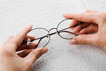 A woman holds black-rimmed glasses against the background of an open textbook reading books in Braille