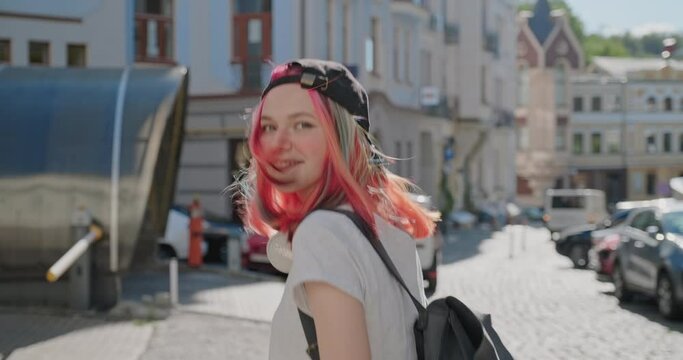 Fashionable beautiful teenager girl with trendy colorful hair walking along street of city, back view