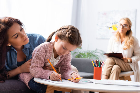 little girl patient drawing picture while visiting psychologist with mother, stock image