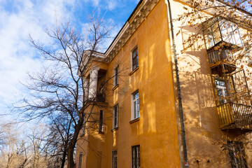 Fototapeta na wymiar bare branches of trees in autumn and part of a yellow large old house against the blue sky.