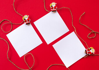 New year's holiday background. White sheets for notes on wooden clothespins with figures of Santa Claus on a red background. Concept of an eco-friendly holiday. Flat lay. Greeting card for Christmas.
