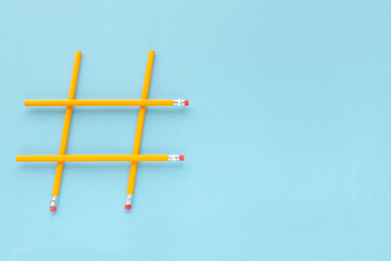 Hashtag sign made from yellow pencils on a blue background with copy space, top view. Wooden yellow pencils on a blue background with copy space. Hashtag is popular on the internet. Minimalism.