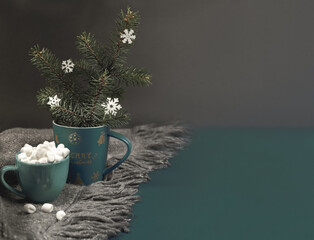 Cozy hugge Christmas background with Xmas mug with fir branches, cup of coffee with marshmallows on grey plaid on dark.