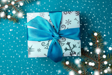 Gift box with DIY bow and fir branches with drawn snow on turquoise backdrop. Christmas background. Top view.