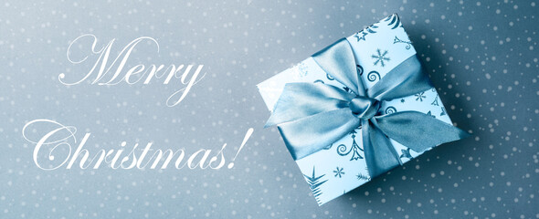 Fototapeta na wymiar Christmas monochrome banner with gift box and caption Merry Christmas on light turquoise backdrop with drawn snow.