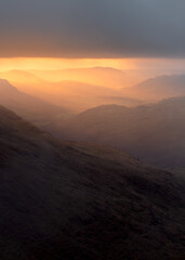 Majestic golden rays of sunlight breaking through clouds, illuminating the Eskdale Valley in the Lake District, UK.