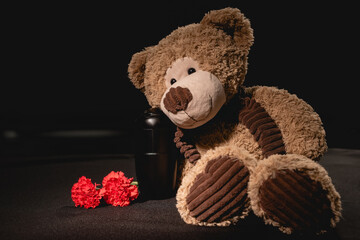 carnation, teddy bear and urn with ashes on black background, funeral 