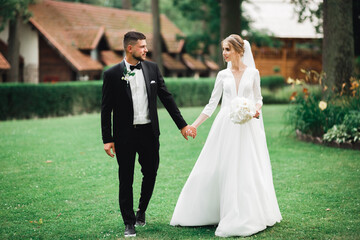 Stylish couple of happy newlyweds walking in the park on their wedding day with bouquet