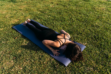 Mujer delgada recostada sobre el césped practica yoga en exteriores por la tarde.