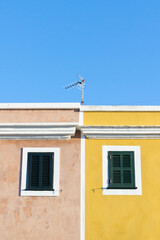 Yellow and pink buildings with green windows. Blue sky in the background.