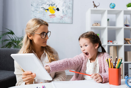 little child screaming and pointing at digital tablet while visiting psychologist, stock image