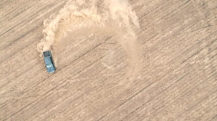 Aerial shot of powerful pickup drifting on dry ground. Black off road vehicle showing performance leaving trace and dust behind. SUV fastly starting ride at the field. Car drive at meadow. Top view