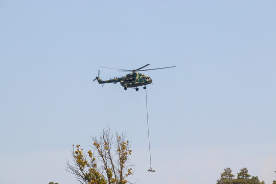 A military helicopter painted in camouflage color is flying high in the sky. Close up. The helicopter carries a military off-road vehicle.