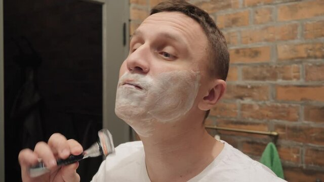 A man puffs out his cheeks while shaving.