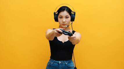 Focused young asian woman with headset and joystic controller playing video games. Isolated on yellow background. High quality photo