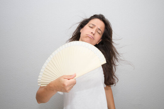 Middle-aged Woman Using Her Paper Fan On An Isolated Gray Background