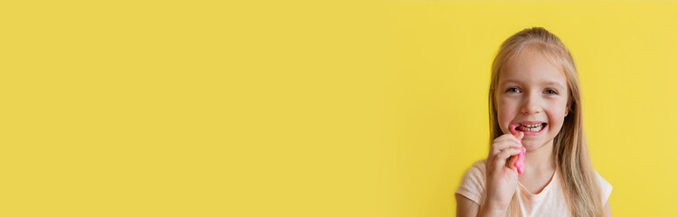 Cute little caucasian girl with blonde hair cleaning teeth with toothbrush on yellow background. Horizontal banner for web design. Studio shot with copy space. Dental hygiene and healthy concept