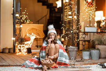 Young woman celebrating alone New Year holidays sitting with sweet gingerbreads on a terrace at home. Concept of quarantine and self-isolation during the epidemic on holidays