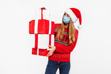 Young happy woman in Christmas Santa Claus hat, in a medical mask on her face, with Christmas gifts, on a white background