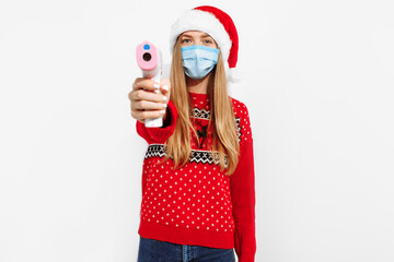 Young woman wearing a Christmas Santa Claus hat and a medical mask on her face, holding an infrared...
