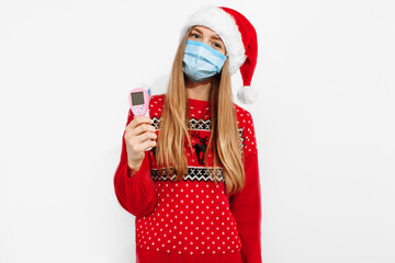 Young woman wearing a Christmas Santa Claus hat and a medical mask on her face, holding an infrared...