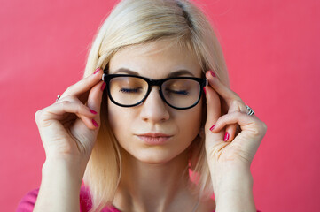 Young woman in a thoughtful pose on a solid background.Portrait of intrigued charming calm and feminine young woman with blond hair putting on eyewear checking sight and lens dioptria.