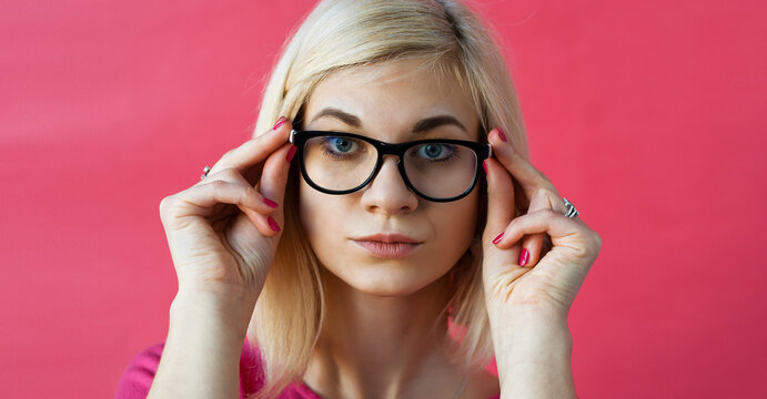 Young woman in a thoughtful pose on a solid background.Portrait of intrigued charming calm and feminine young woman with blond hair putting on eyewear checking sight and lens dioptria.
