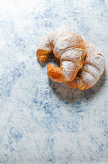 Two freshly baked croissants with icing sugar on a blue background with texture