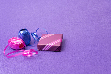 Gift in a purple box and decorative ribbon on a purple background.