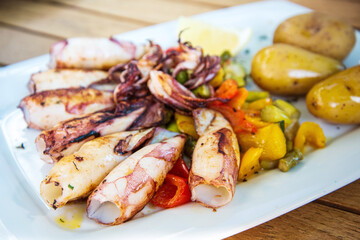 Delicious grilled whole squid with tomatoes, cucumber slices, Beetroots pieces and green dandelions served in white plate for a healthy Mediterranean meal