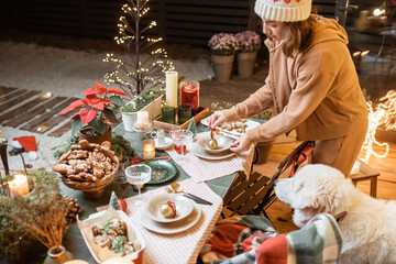 Woman serving and decorating a festive dinner table on the christmas eve outdoors on the terrace