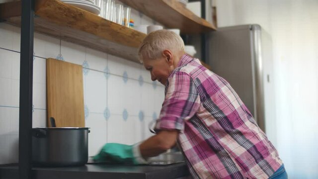 Tired mature woman cleaning cooking top in kitchen