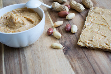 Peanut butter and peanuts on wooden background