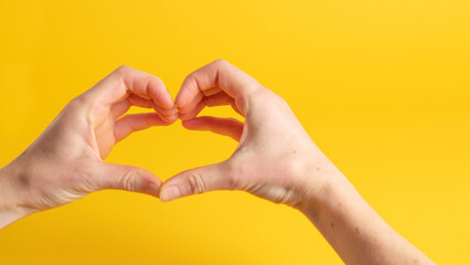 Two hand forming a heart shape with the fingers. Heart shaped hands on yellow background. Hands making a heart