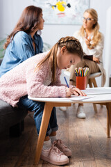 little girl patient drawing picture while visiting psychologist with mother, stock image
