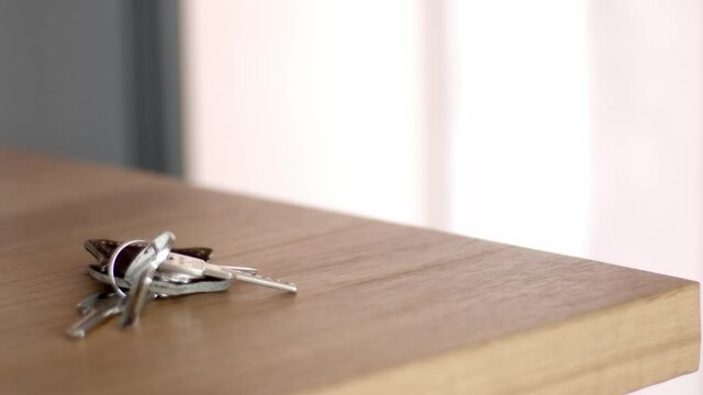 A hand in a beige jacket opens the door on the background, throws the keys from the apartment on the wooden table and closes the door from the inside. 4k close up video, still high quality footage.