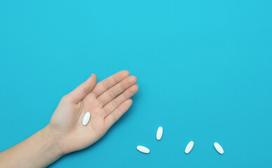 Pill on hand and some pills on blue background. Medicine concept.