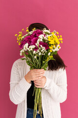 Caucasian woman covering her face with bouquet of flowers on pink