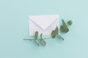 White envelope with twig and leaves lying on pale blue background