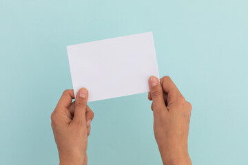 Two hands of caucasian woman holding white paper over pale blue background