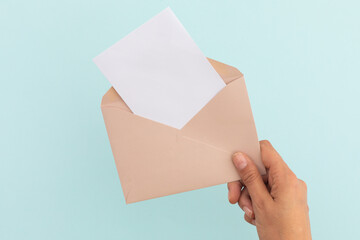 Hand of caucasian woman holding opened envelope with letter over pale blue background