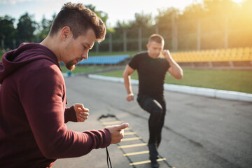personal trainer with stopwatch measuring time of male exercising outdoor - Powered by Adobe