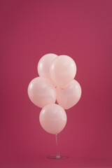 Bunch of five pale pink balloons floating on dark red background